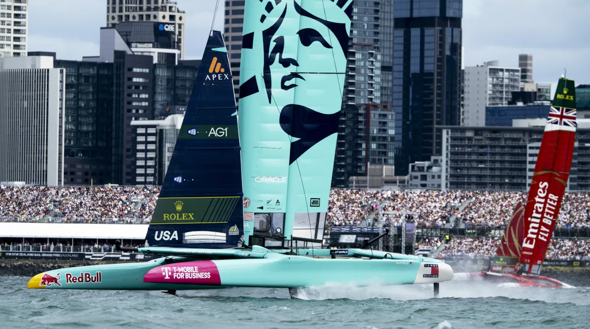 The US SailGP team's boat racing past a packed waterfront, with the AG1 logo on its sail