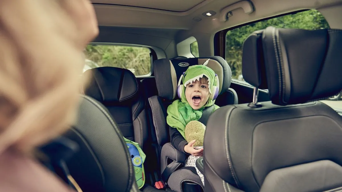 A child in a dinosaur costume riding in Renault's family car.