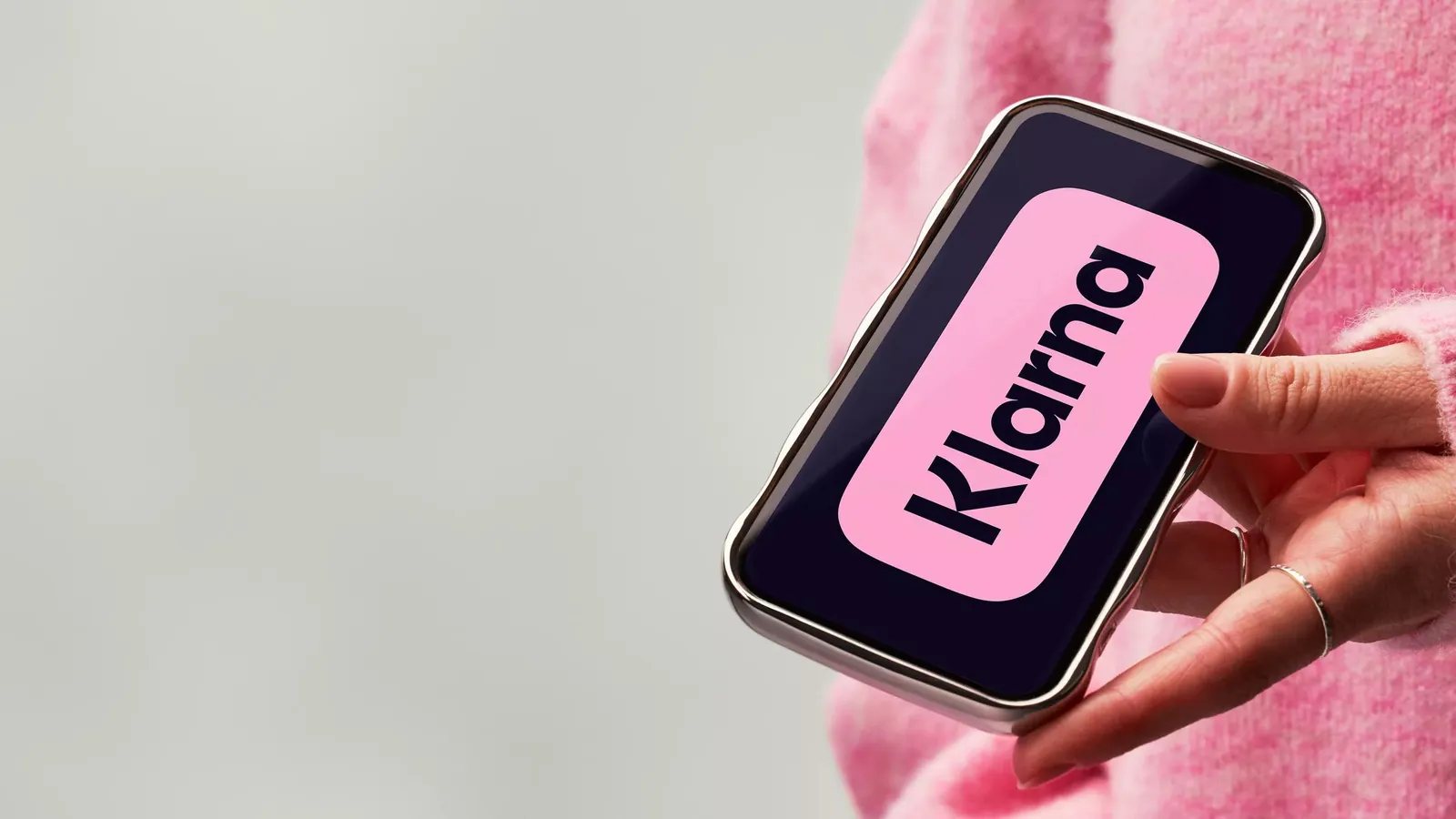A phone showing the Klarna logo, held by someone in a pink sweater.