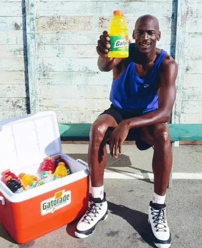 An athlete holding up a Gatorade next to a Gatorade cooler