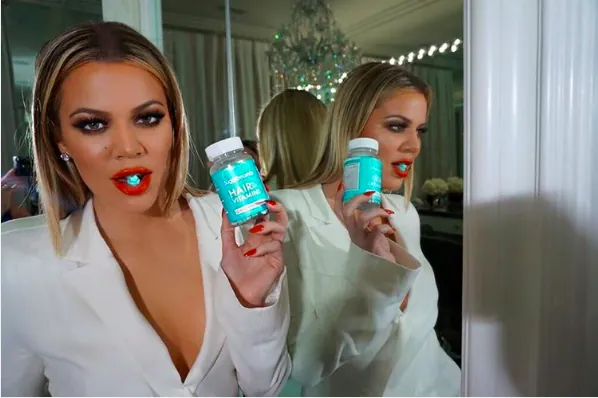 Khloé Kardashian holding the SugarBearHair bottle in a mirror selfie.