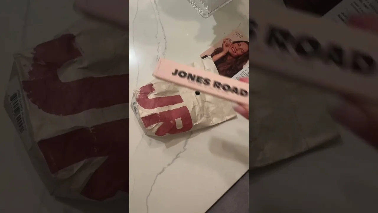 a real creator's torn-open Jones Road kraft seeding bag on a marble counter, next to a promo card