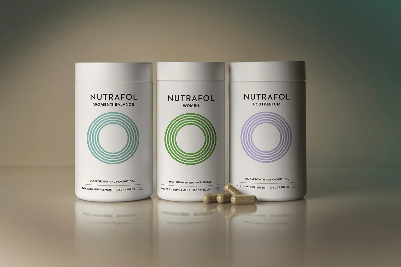 three real Nutrafol supplement bottles with loose capsules, the product behind the cases it seeds to salons