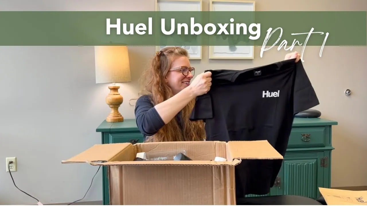 a real creator pulling a black Huel t-shirt out of an open shipping box on camera