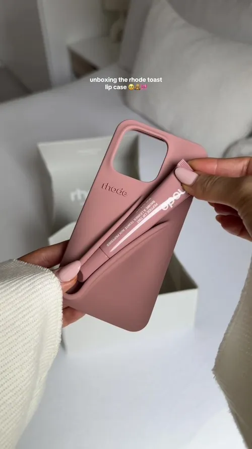 A dusty pink rhode phone case with a moulded slot on the back holding a matching Peptide Lip Tint tube