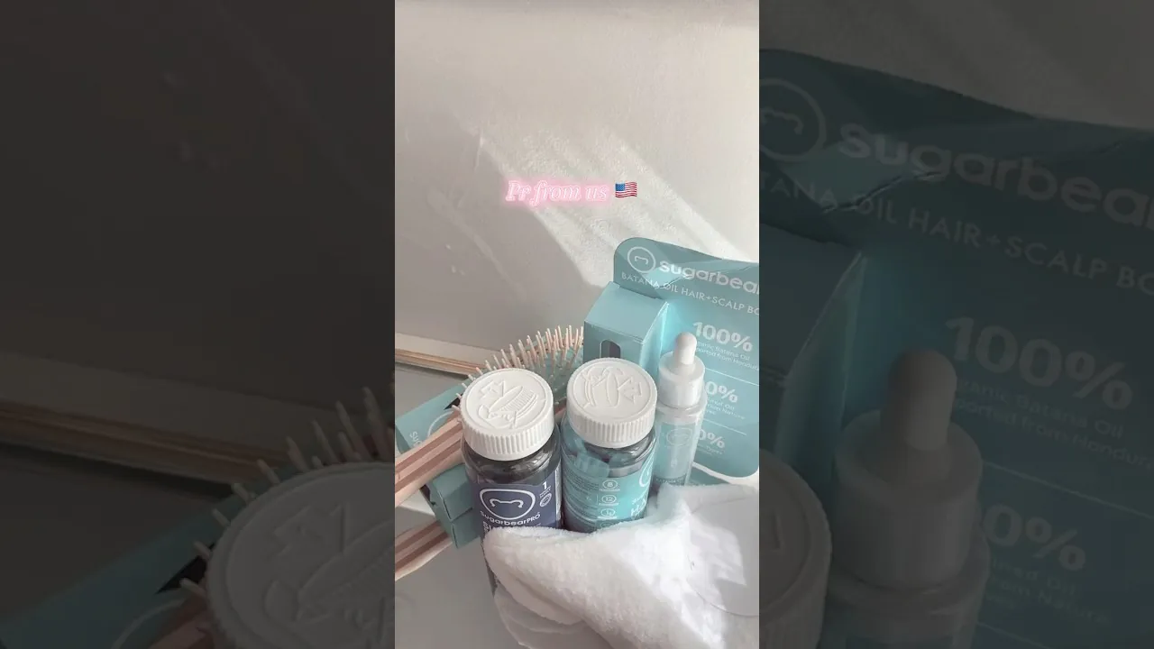 a SugarBearHair PR box from a creator's unboxing: two vitamin bottles, a Batana Oil Hair and Scalp box, a wooden brush and a dropper bottle