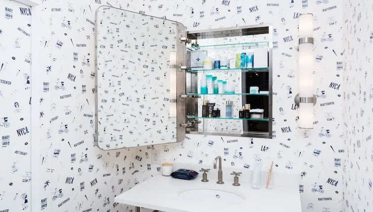 A bathroom with patterned wallpaper and a mirrored cabinet