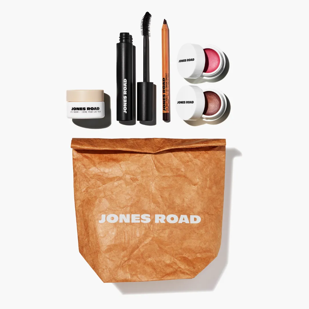 Jones Road's own kraft-paper seeding bag, laid out with the Hero Kit: eye cream, mascara, brow pencil, two Miracle Balms
