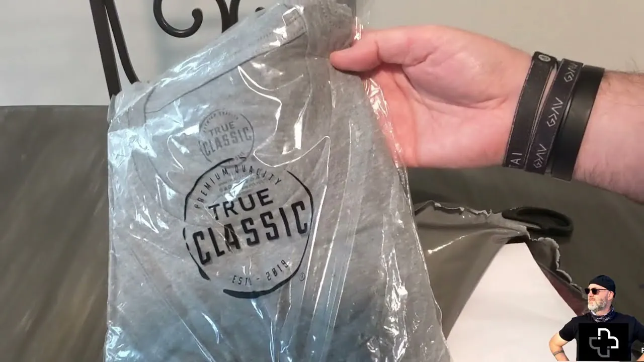 a hand holding a real True Classic shirt still sealed in its poly bag