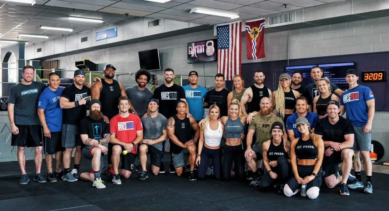 About 30 people in 1st Phorm shirts posed together in a gym