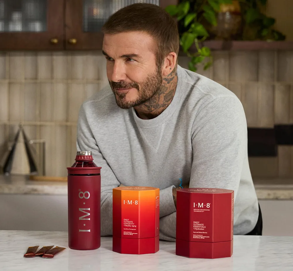 David Beckham leaning on a kitchen counter beside IM8 bottles and boxes