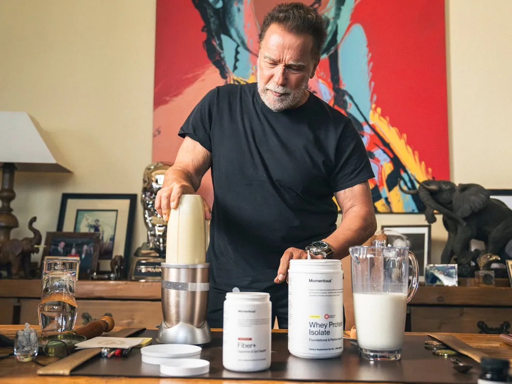 Arnold Schwarzenegger mixing a shake at home beside Momentous tubs