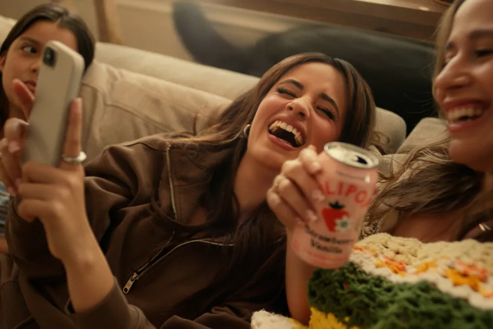 Camila Cabello laughing on a couch with a can of Olipop Strawberry Vanilla