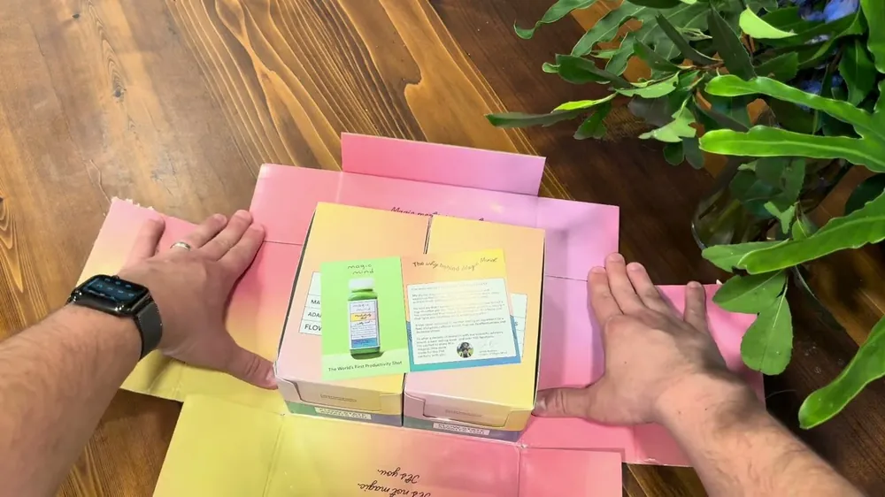 Two hands opening a Magic Mind box, with the mailer, two cartons and a founder&rsquo;s story card